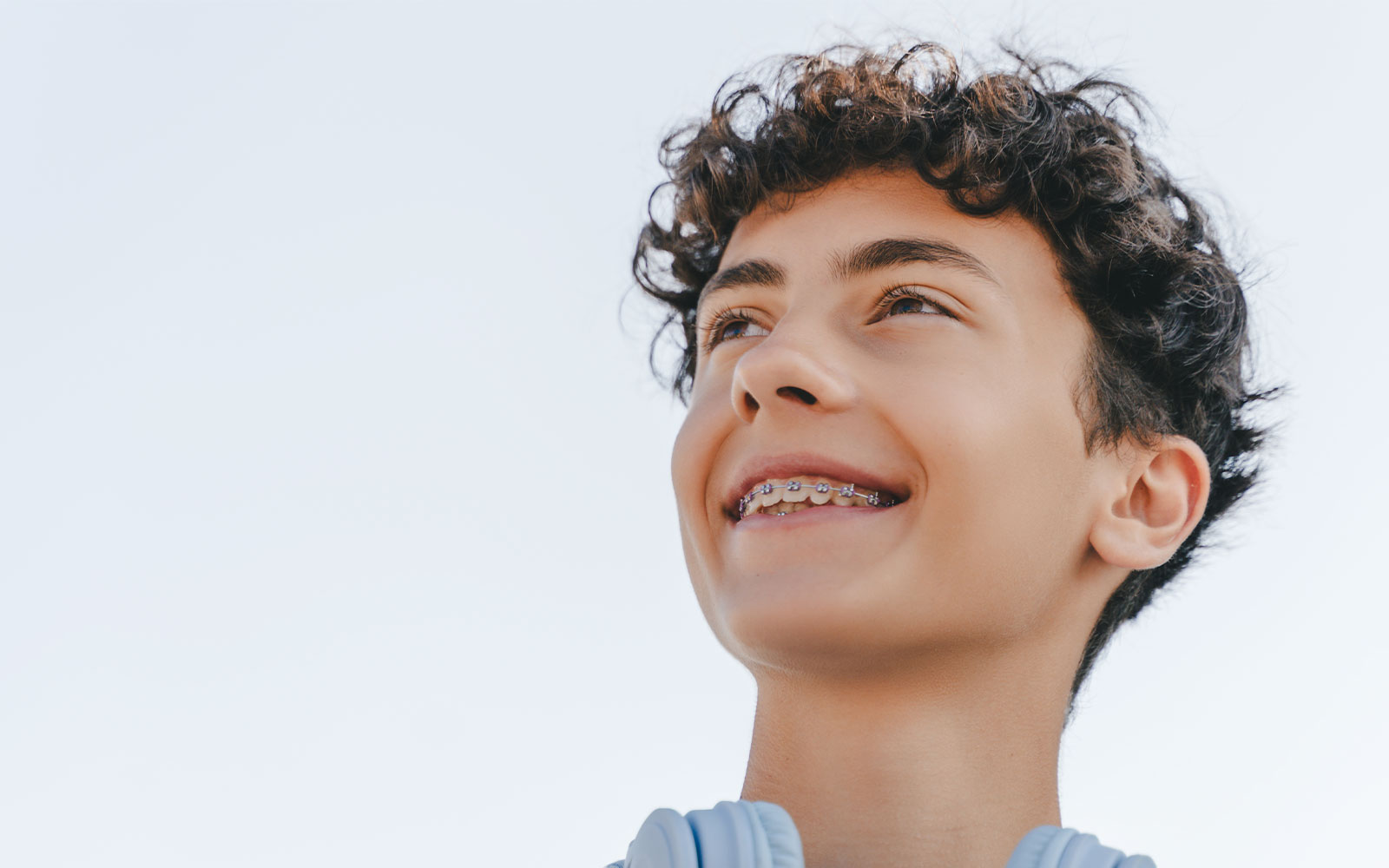 The image shows a young person with curly hair smiling at the camera, wearing a light-colored top against a neutral background.