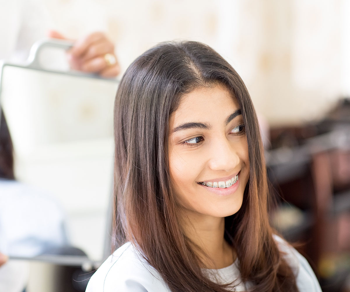 A woman with long hair smiling at a camera while sitting in a salon chair.